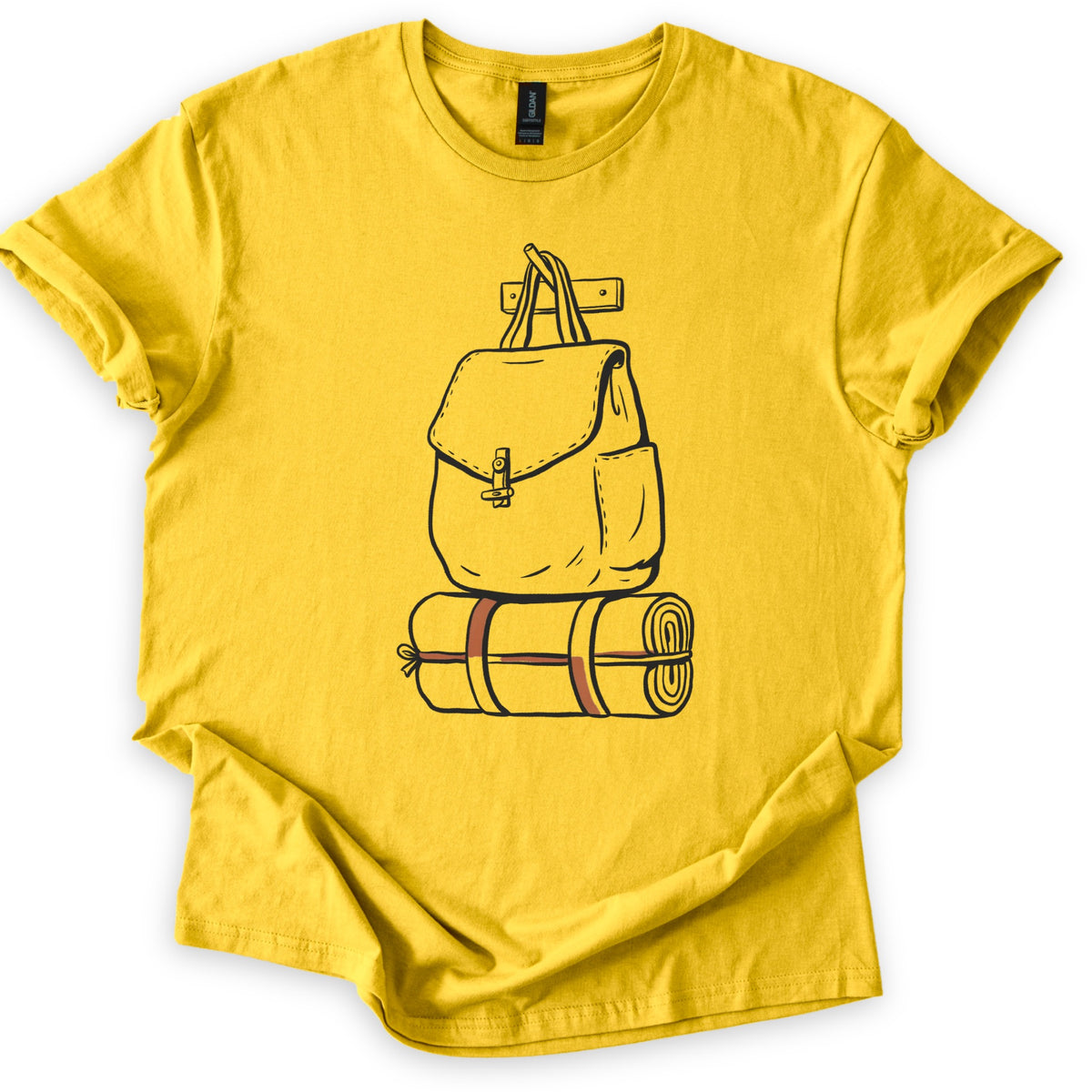 Backpack And Bedroll Comfort Colors T-shirt in Daisy, laid flat. A black line drawing of a canvas backpack with a toggle-clasp flap hangs by its handles from a wall peg above a rolled bedroll tied with rust-red straps. No words. Cuffed sleeves on a white surface.