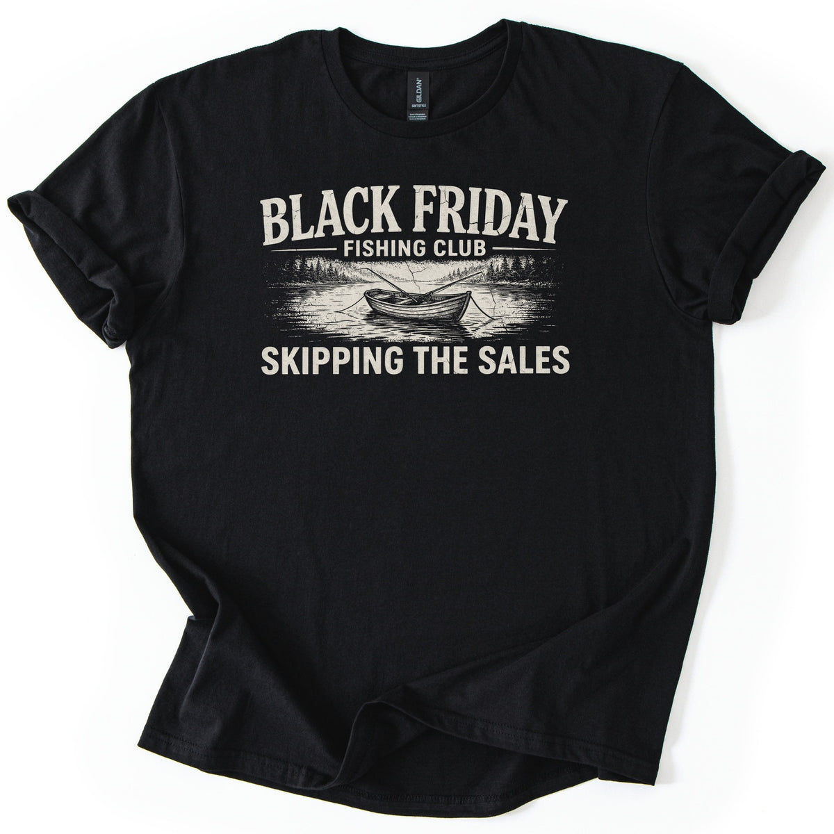 Black Friday Fishing Club Comfort Colors T-shirt in Black, laid flat. A cream sketch of a rowboat with two fishing rods on a pine-lined lake sits between the words Black Friday Fishing Club and Skipping the Sales. The sleeves are rolled on a white background.