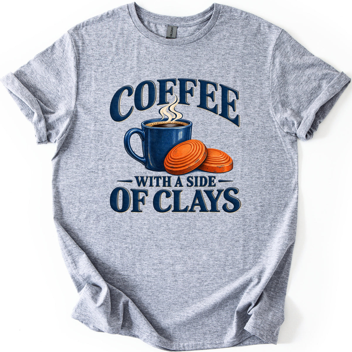 Coffee with a Side of Clays Comfort Colors T-shirt in Sport Grey, laid flat. Navy text reads COFFEE over a steaming blue speckled mug and two orange clay pigeons, then WITH A SIDE OF CLAYS underneath. The shirt is spread on a white surface with rolled sleeves.