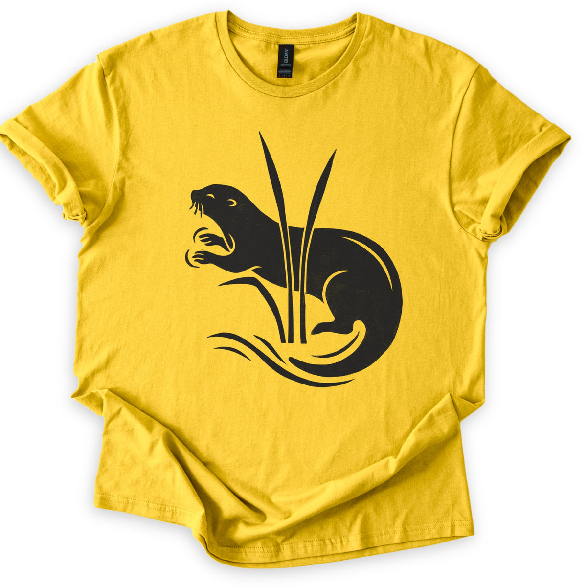 Otter In The Reeds Comfort Colors T-shirt in Daisy, laid flat. A black silhouette of an otter with open mouth, whiskers and raised paws curls behind two tall reeds above swirling water lines. No words. The shirt lies on a white surface with sleeves rolled.