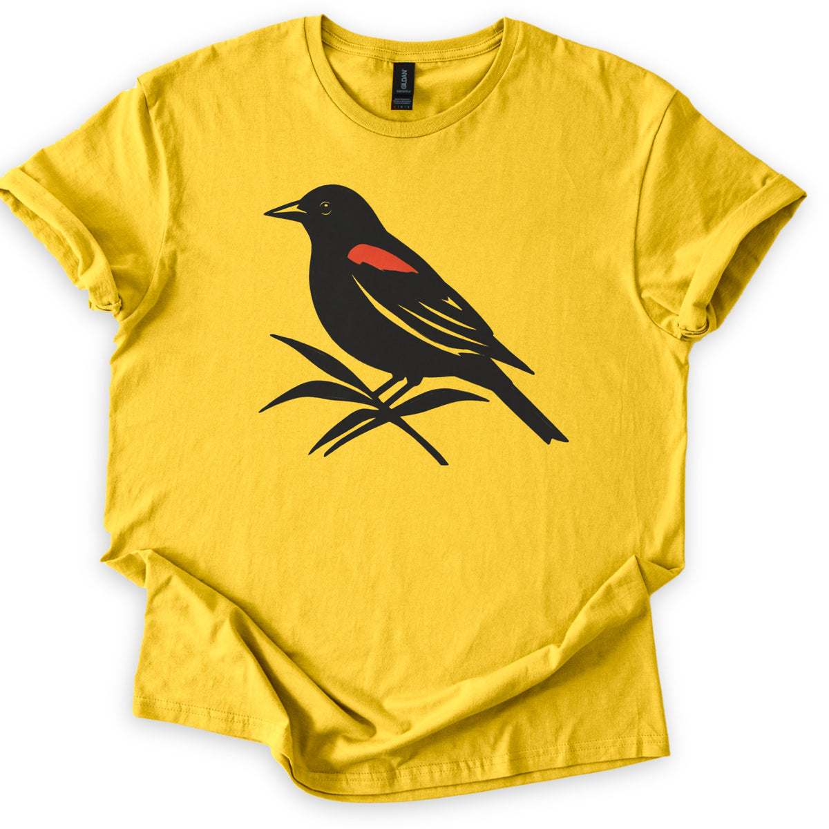 Red Winged Blackbird Comfort Colors T-shirt in Daisy, laid flat. A black silhouette of a red-winged blackbird with a red shoulder patch, perched on slender leaves, with no words. The shirt has rolled sleeves and lies on a white background.