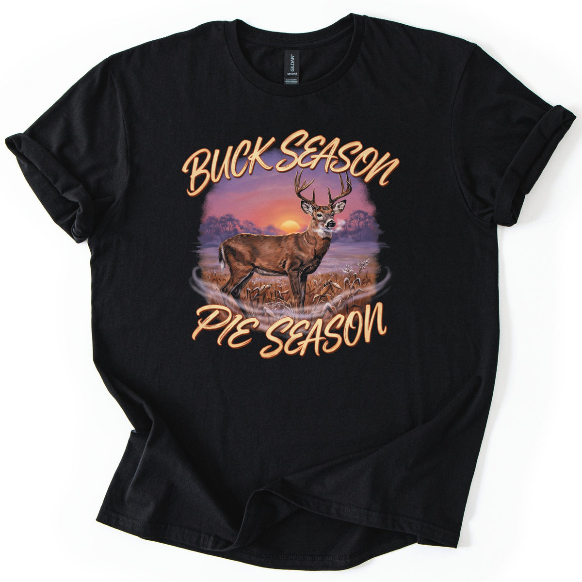 Buck Season Pie Season Comfort Colors T-shirt in Black, laid flat. Peach script reads Buck Season above and Pie Season below a painted whitetail buck in a frosty cornfield, with an orange sun setting behind trees. The sleeves are cuffed, on a white background.
