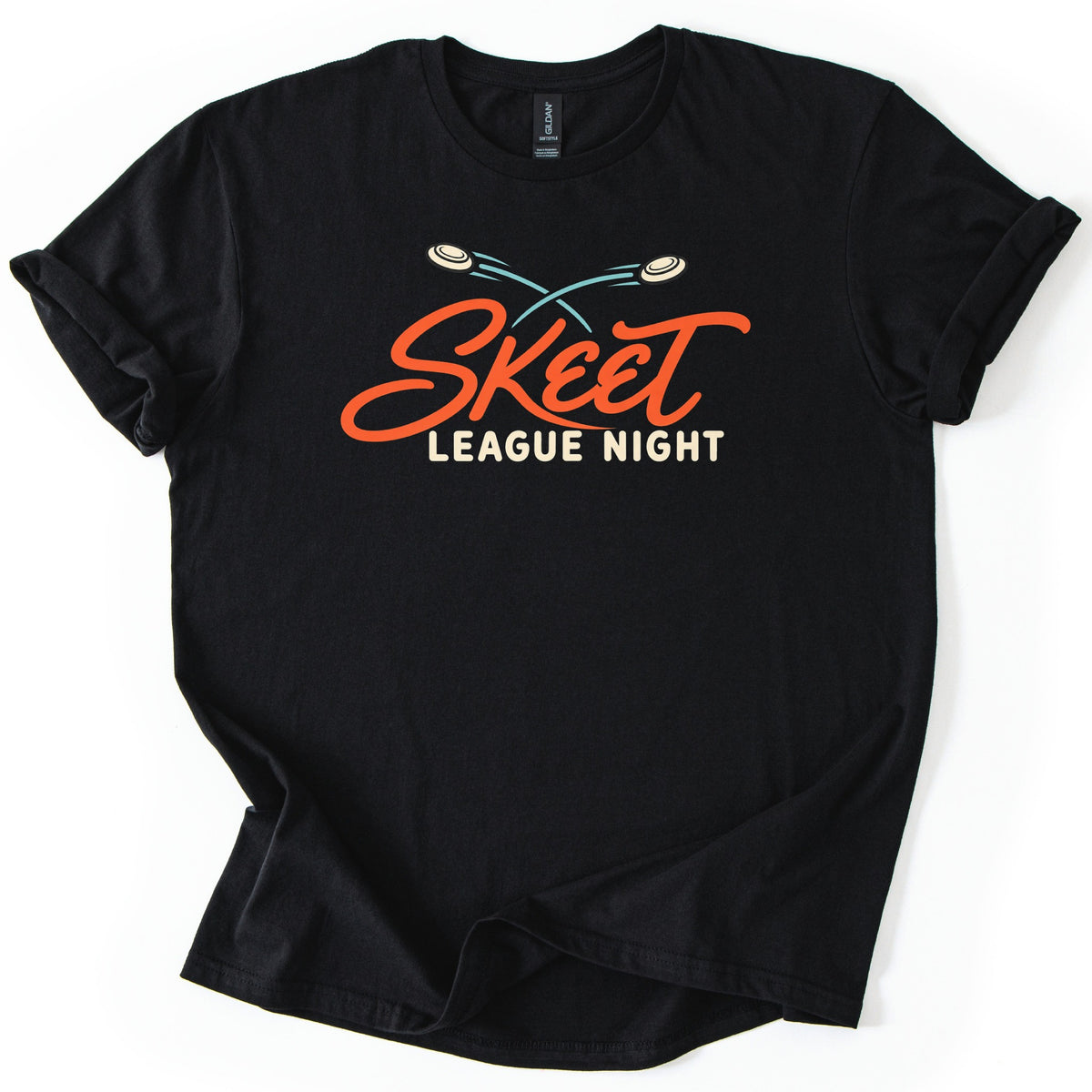 Skeet League Night Comfort Colors T-shirt in Black, laid flat. Two cream clay targets with crossing teal trails fly above the word Skeet in orange script, with League Night in cream capitals below. The shirt has rolled sleeves on a white background.