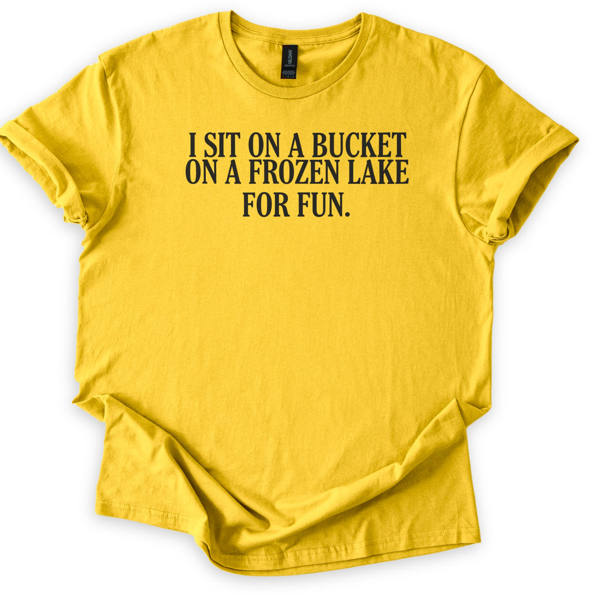Bucket On A Frozen Lake Comfort Colors T-shirt in Daisy, laid flat. Black serif capital letters across the chest read I SIT ON A BUCKET ON A FROZEN LAKE FOR FUN. The shirt lies on a white surface with its sleeves rolled and the hem loosely folded.