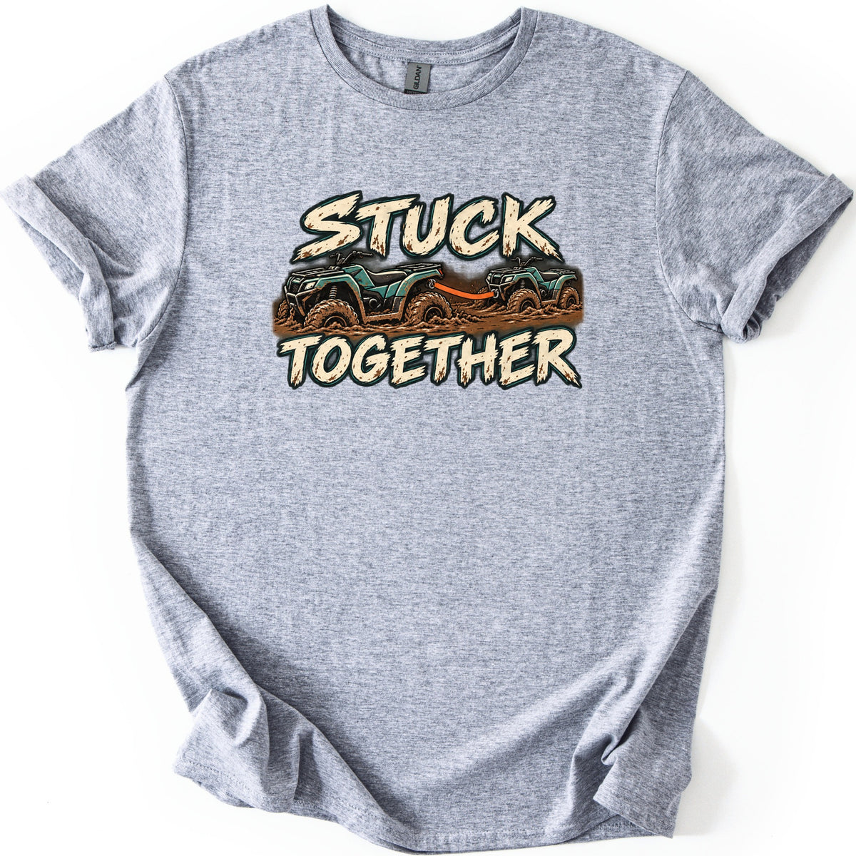 Stuck Together Comfort Colors T-shirt in Sport Grey, laid flat. Two mud-covered green ATVs joined by an orange tow strap sit between the words Stuck Together in distressed cream letters. The shirt has cuffed sleeves and lies on a white background.