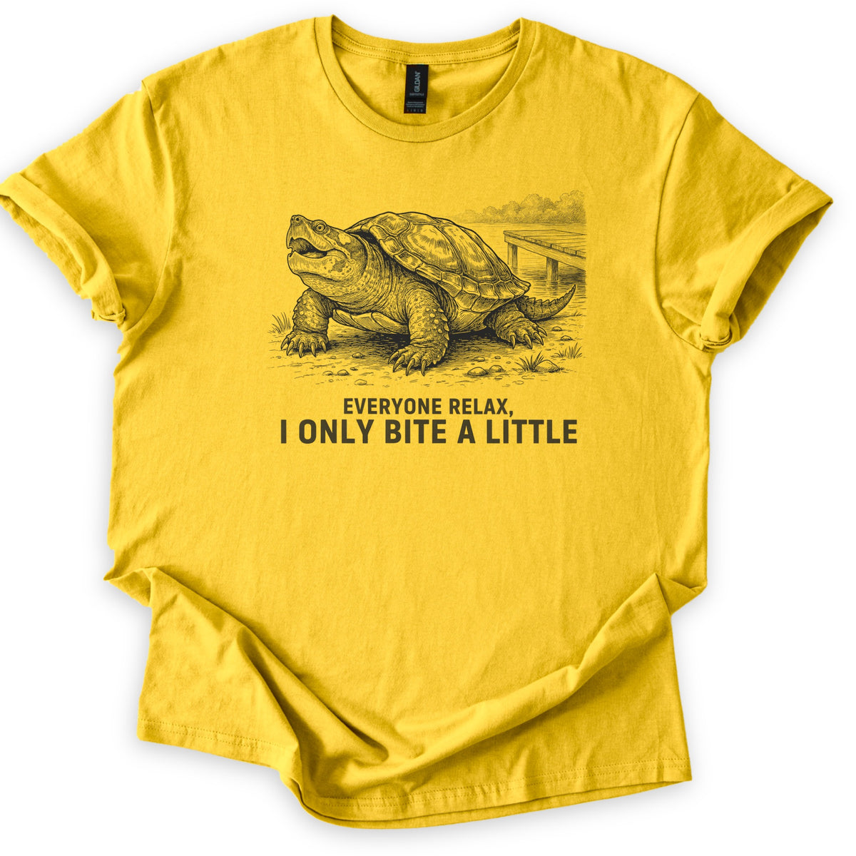 Everyone Relax I Only Bite A Little Comfort Colors T-shirt in Daisy, laid flat. A black ink drawing of a snapping turtle with its mouth open on a shoreline by a wooden dock, above the words Everyone Relax, I Only Bite A Little. Sleeves are rolled on a white background.