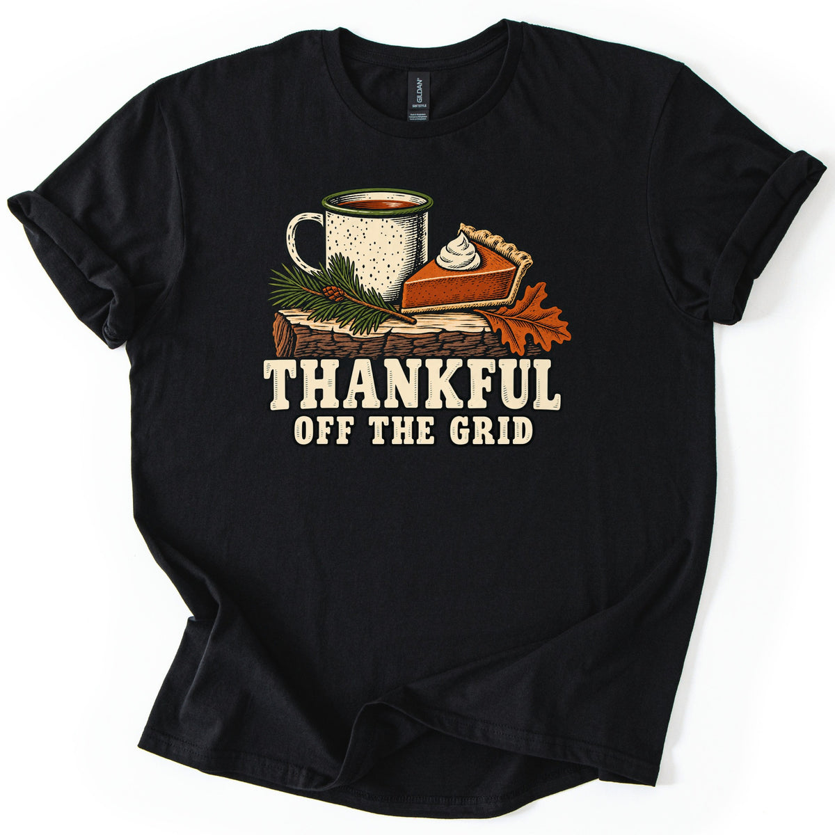 Thankful Off the Grid Comfort Colors T-shirt in Black, laid flat. A speckled enamel camp mug, a slice of pumpkin pie topped with whipped cream, a pine sprig and an orange oak leaf rest on a log above the words Thankful Off the Grid. Sleeves are cuffed on a plain white background.