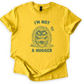 I'm Not A Hugger Comfort Colors T-shirt in Daisy, laid flat. A scowling sketch-style hedgehog with crossed arms, a butterfly beside it, sits between the words I'm Not A Hugger in dark green. The sleeves are rolled on a white background.
