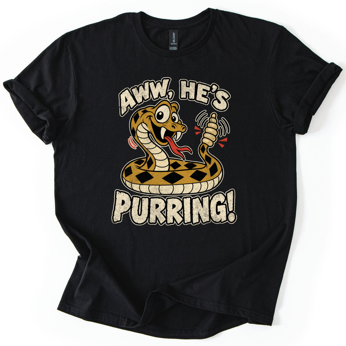 Aww He's Purring Comfort Colors T-shirt in Black, laid flat. A coiled cartoon rattlesnake with tan and black diamond markings sticks out its tongue and shakes its rattle under Aww, He's and above Purring! The shirt lies on a white background.