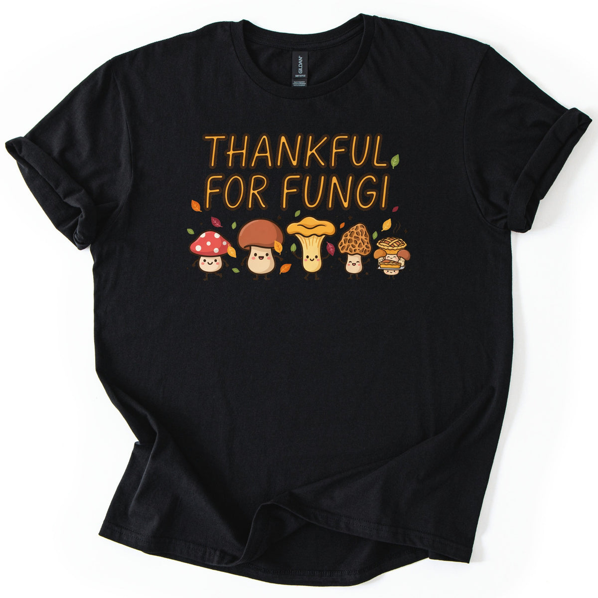 Thankful For Fungi Comfort Colors T-shirt in Black, laid flat. The words Thankful For Fungi in orange letters above five smiling cartoon mushrooms, one holding a pie, with autumn leaves around them. The shirt has rolled sleeves on a white background.