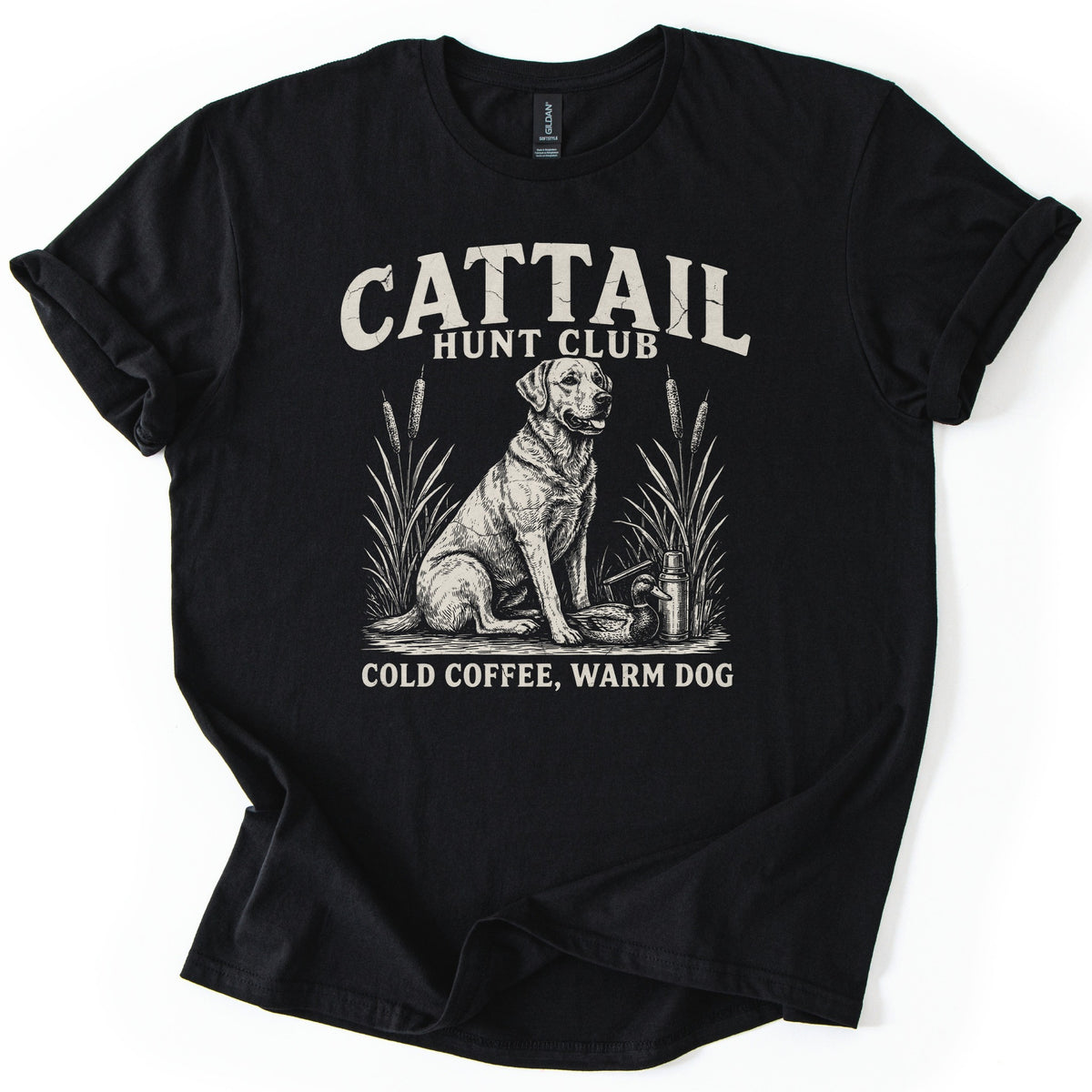 Cattail Hunt Club Comfort Colors T-shirt in Black, laid flat. Distressed cream lettering reads Cattail Hunt Club over a sketched Labrador retriever with cattails, a duck decoy and a thermos, then Cold Coffee, Warm Dog. Sleeves rolled, on a white background.