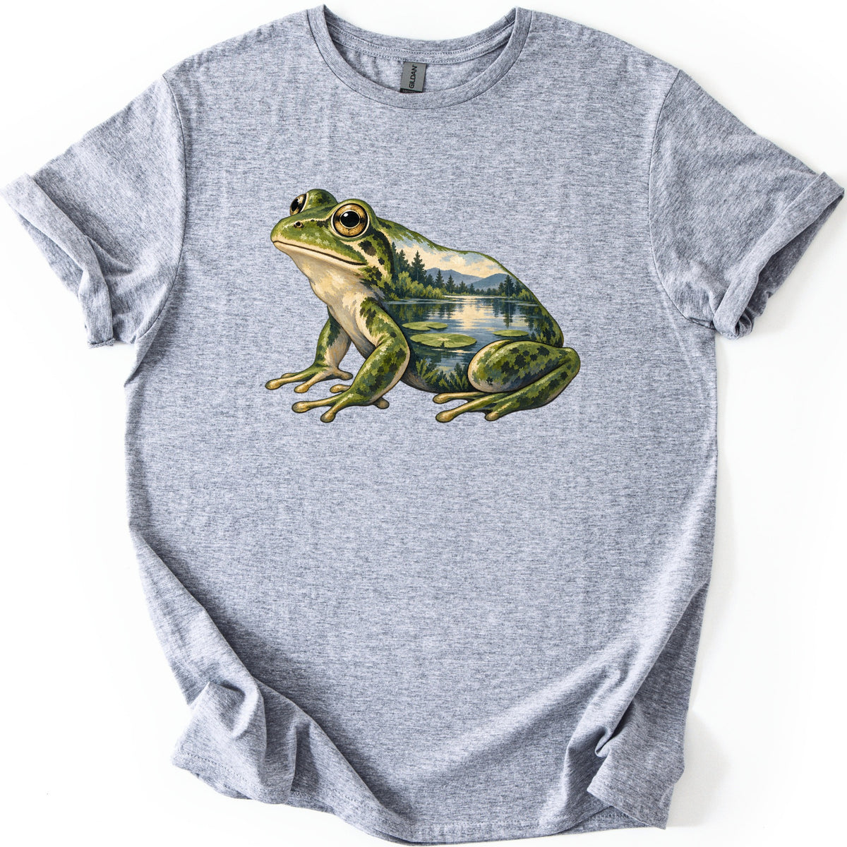 Lily Pond Frog Comfort Colors T-shirt in Sport Grey, laid flat. A painted green frog sits in profile, its body filled with a lake scene of pine trees, mountains and lily pads. No words are printed. The heathered shirt has cuffed sleeves on a white background.