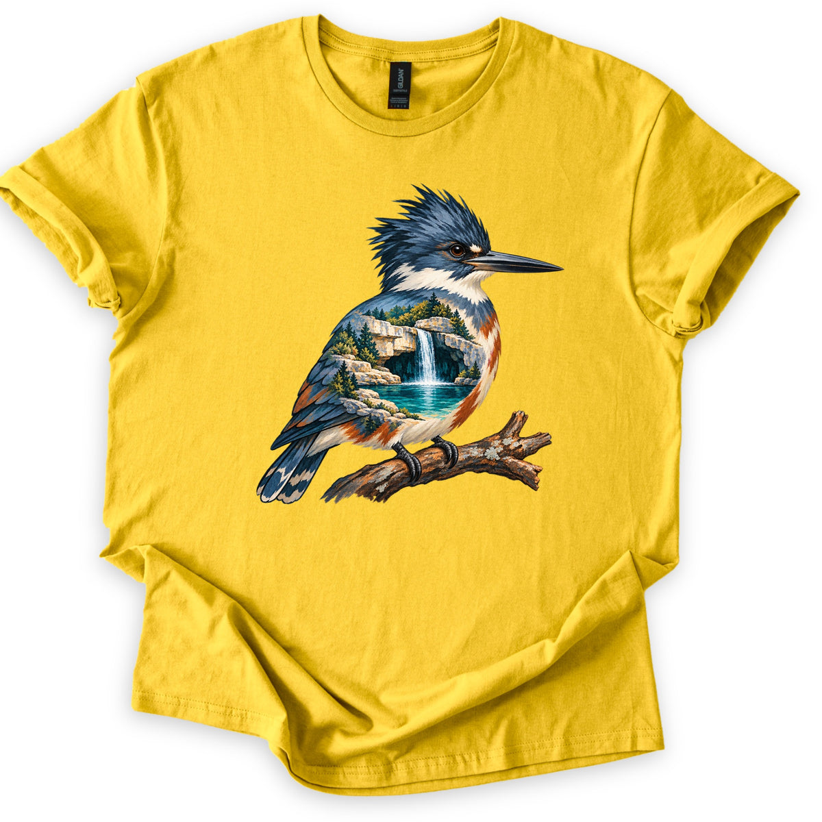 Kingfisher Waterfall Comfort Colors T-shirt in Daisy, laid flat. A painted kingfisher with a blue crest perches on a branch, its body filled with a waterfall pouring into a turquoise pool among rocks and pine trees. No words. Sleeves rolled, on a white background.