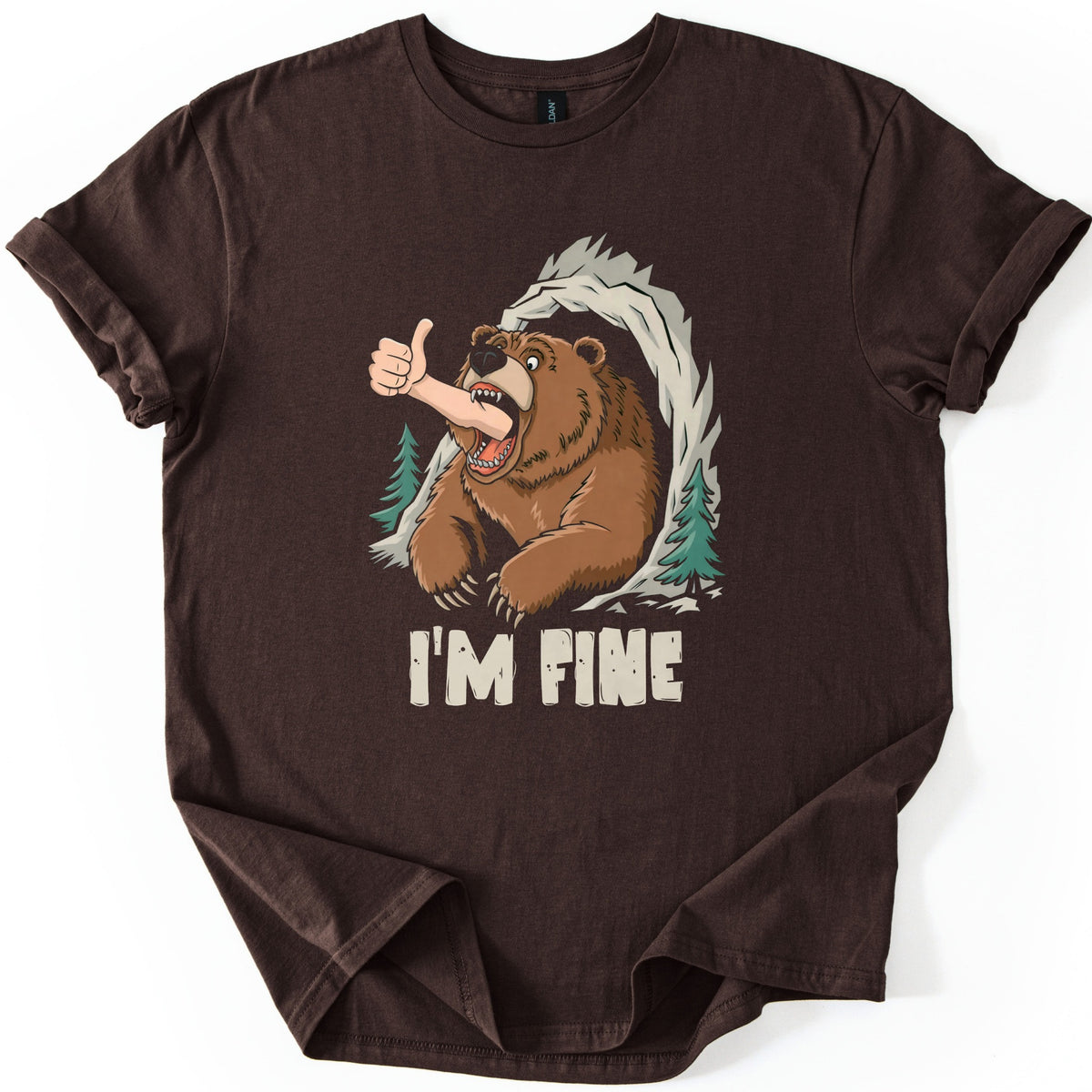 Grizzly I'm Fine Comfort Colors T-shirt in Dark Chocolate, laid flat. A cartoon grizzly bear bursts from a rocky cave between pine trees, a human arm giving a thumbs up sticking out of its open jaws, above the words I'M FINE. The shirt has rolled sleeves on a white surface.