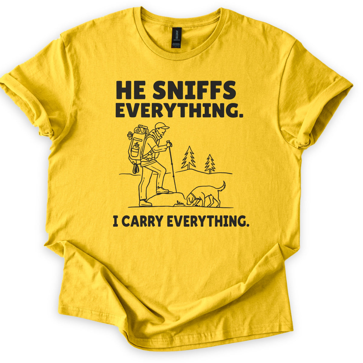 Trail Dog Pack Mule Comfort Colors T-shirt in Daisy, laid flat. Black line art of a hiker with a loaded backpack and trekking pole stepping onto a rock as a dog sniffs the ground, with pine trees behind, between the words He sniffs everything. and I carry everything. Sleeves rolled, on white.