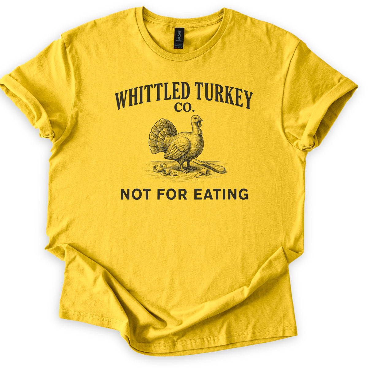 Whittled Turkey Co Comfort Colors T-shirt in Daisy, laid flat. Dark print of an engraved-style turkey beside wood shavings and a carving knife, under the words Whittled Turkey Co. and above Not For Eating. Sleeves are cuffed on a white background.