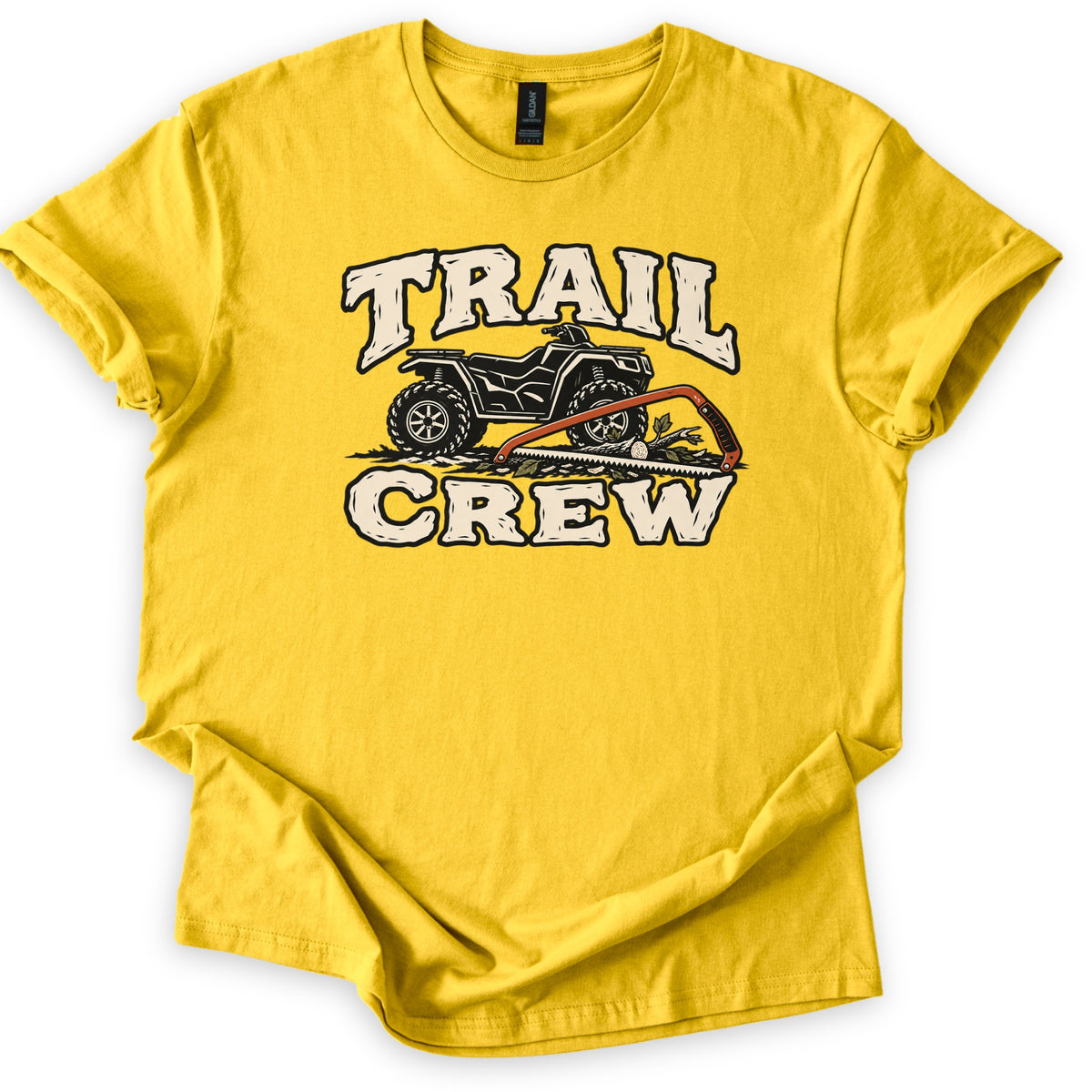Trail Crew Comfort Colors T-shirt in Daisy, laid flat. A black ATV sits between the cream words TRAIL and CREW, with an orange bow saw lying across a cut branch and leaves in front. The shirt is spread on a white background with its sleeves rolled.