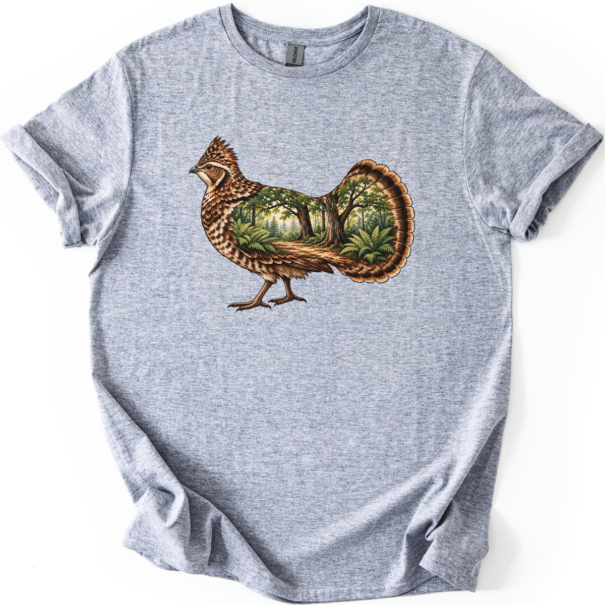 Ruffed Grouse Woods Comfort Colors T-shirt in Sport Grey, laid flat. A walking ruffed grouse with a crested head and barred brown feathers, its body and fanned tail filled with a forest scene of trees, ferns and a dirt path. No words. Sleeves rolled, on a white background.