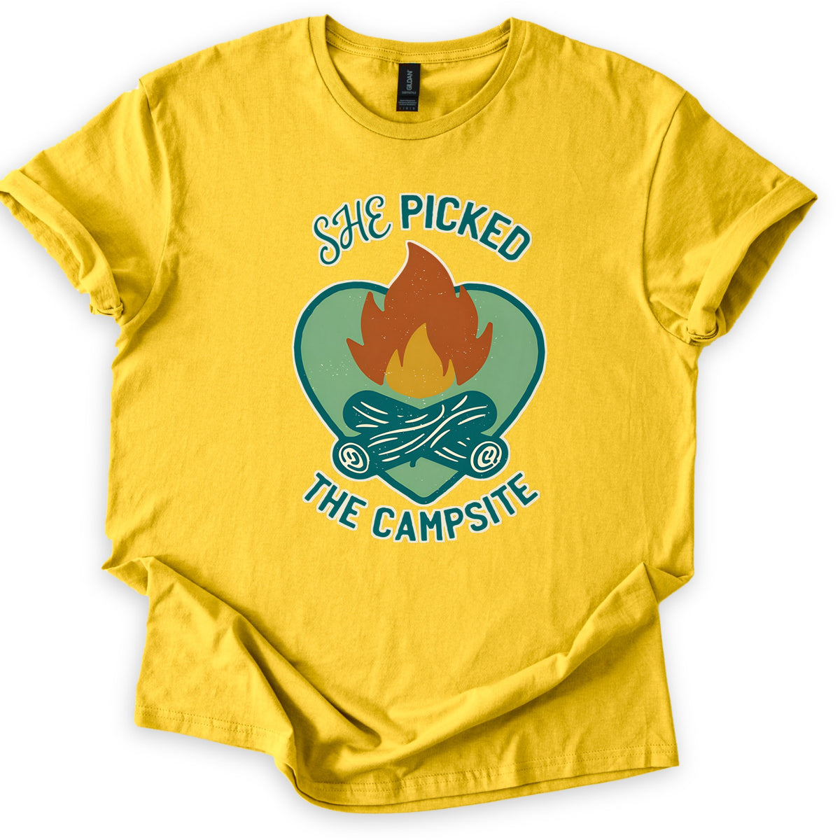 She Picked The Campsite Comfort Colors T-shirt in Daisy, laid flat. An orange and yellow campfire on crossed teal logs inside a sage green heart, with the words SHE PICKED above and THE CAMPSITE below. The shirt lies on a white surface with cuffed sleeves and a folded hem.