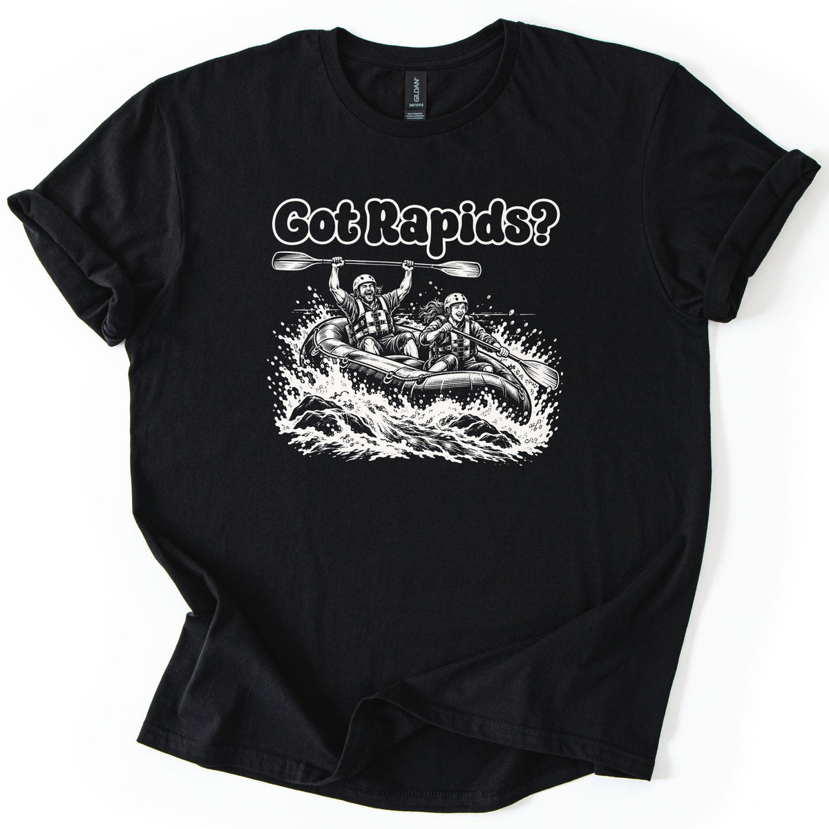 Got Rapids Comfort Colors T-shirt in Black, laid flat. White line art shows a man raising a paddle overhead and a smiling woman paddling a raft through splashing whitewater, under the words Got Rapids? The sleeves are rolled on a white background.
