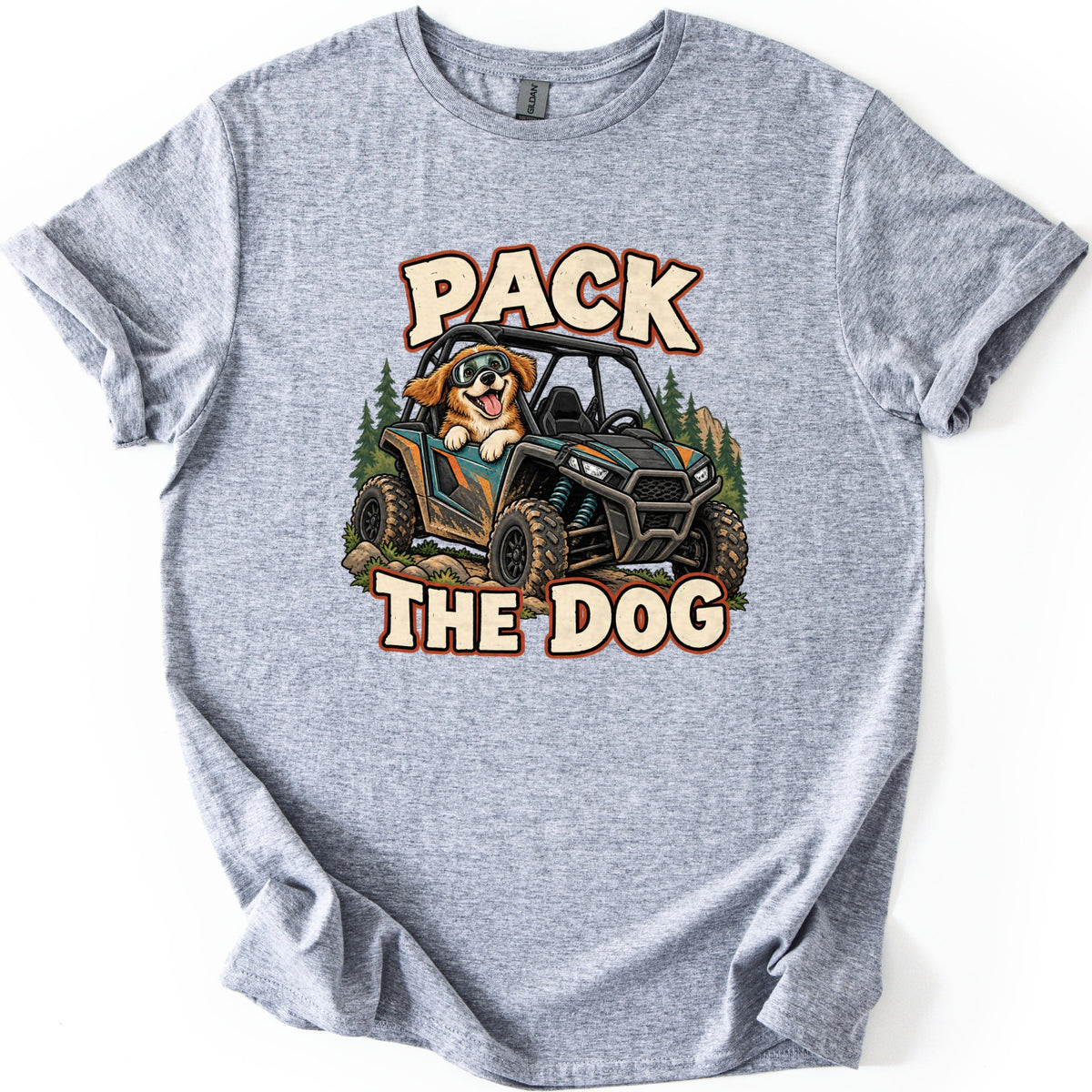 Pack the Dog Comfort Colors T-shirt in Sport Grey, laid flat. A cartoon dog in goggles rides a muddy teal and black side-by-side UTV past pine trees, between the words PACK and THE DOG in cream letters. The shirt has cuffed sleeves on a white background.