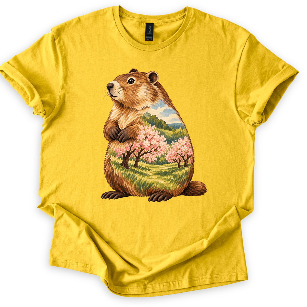 Groundhog Blossom Meadow Comfort Colors T-shirt in Daisy, laid flat. A painted groundhog sits upright with paws at its chest, its body filled with a meadow of pink blossoming trees, green hills and blue sky. No words. Sleeves cuffed, on a white background.