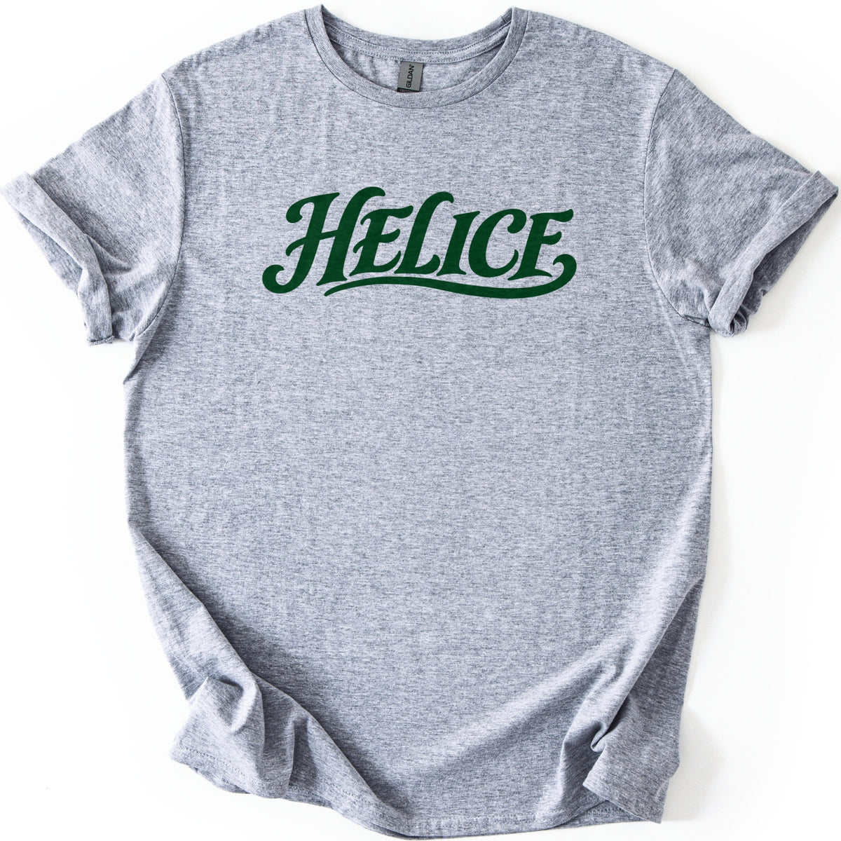 Helice Comfort Colors T-shirt in Sport Grey, laid flat. The word Helice is printed across the chest in dark green retro script with a swooping underline tail. The heathered shirt lies on a white background with its sleeves cuffed and the hem loosely folded.