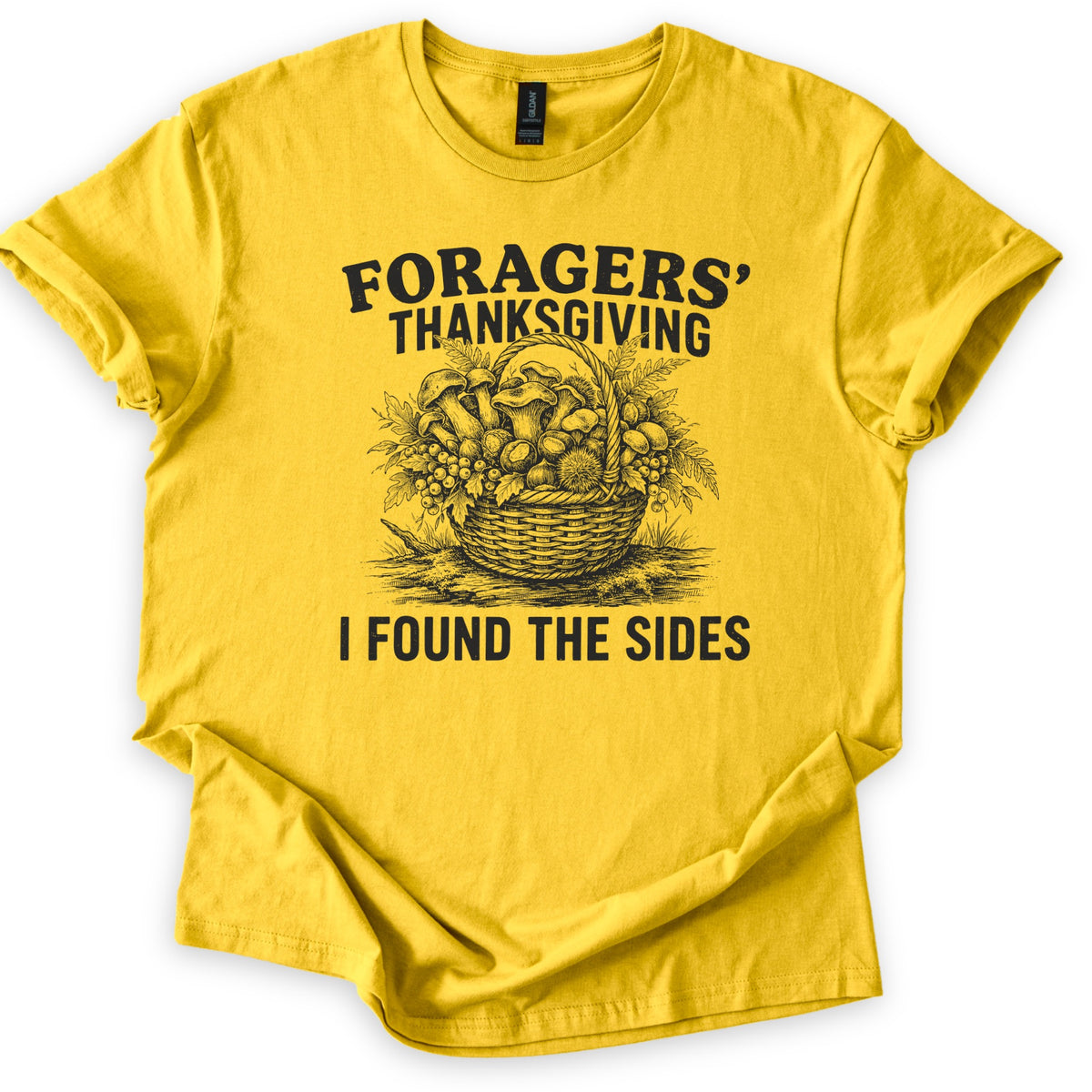 Foragers Thanksgiving Comfort Colors T-shirt in Daisy, laid flat. Black sketch of a wicker basket of mushrooms, berries, ferns and a chestnut burr, between the words Foragers' Thanksgiving and I Found the Sides. Sleeves cuffed, on a white background.