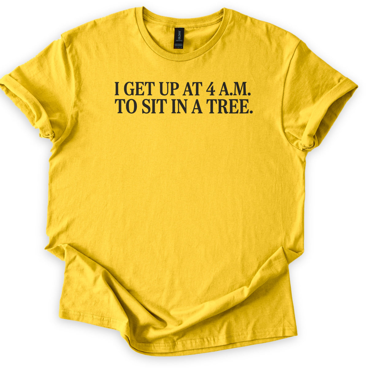 Sit In A Tree Comfort Colors T-shirt in Daisy, laid flat. Black serif capital letters across the chest read I GET UP AT 4 A.M. TO SIT IN A TREE. on two lines. The shirt lies on a white surface with its sleeves rolled and the hem loosely folded.