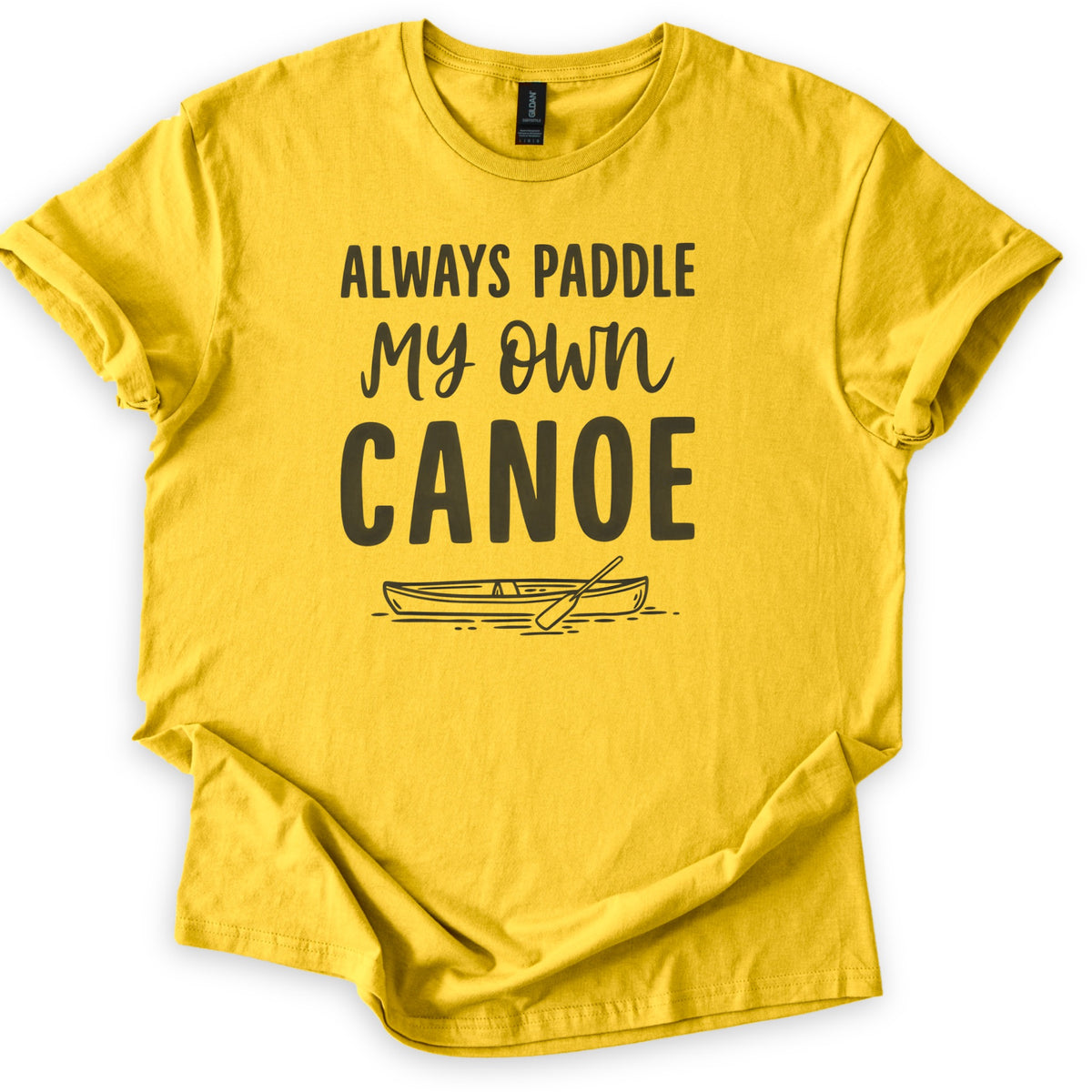 Paddle My Own Canoe Comfort Colors T-shirt in Daisy, laid flat. Dark charcoal text reads Always Paddle My Own Canoe above a line drawing of a canoe with a paddle on rippling water. The shirt has rolled sleeves and lies on a white surface.