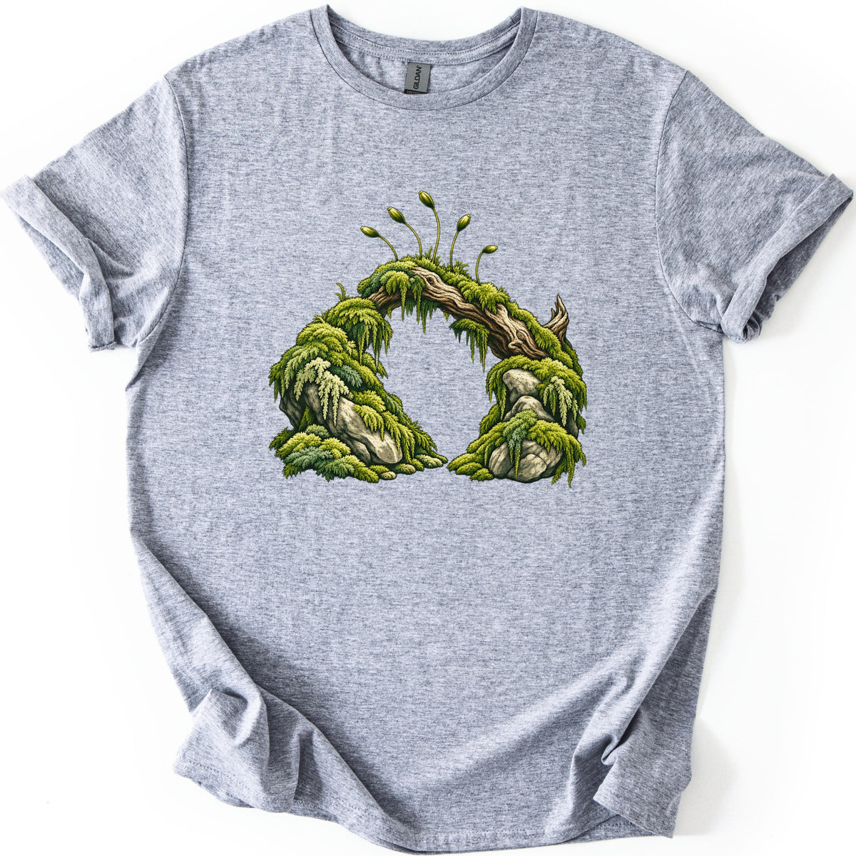 Moss Arch Comfort Colors T-shirt in Sport Grey, laid flat. A moss-covered log bridges two mossy gray boulders to form an arch, with thin spore stalks sprouting on top. No words are printed. The shirt lies on a white background with its sleeves rolled.