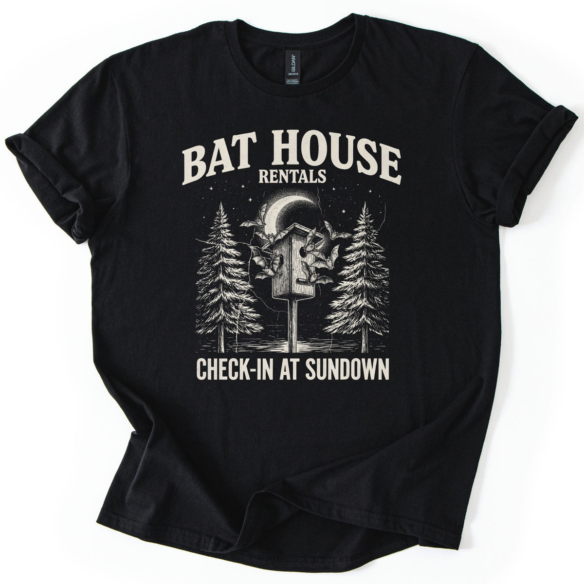 Bat House Rentals Comfort Colors T-shirt in Black, laid flat. Cream text reads Bat House Rentals over an etched drawing of bats flying around a wooden bat house on a post, a crescent moon and two pine trees, with Check-In at Sundown below. Sleeves cuffed, on white.