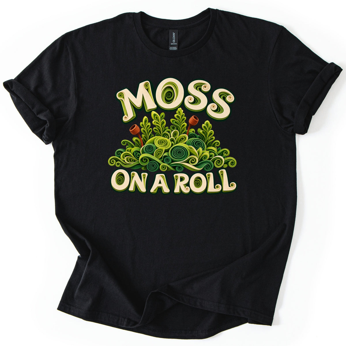Moss on a Roll Comfort Colors T-shirt in Black, laid flat. A mound of green moss made of quilled paper spirals and fronds, with two rust-brown spore capsules, sits between cream letters reading MOSS and ON A ROLL. Sleeves are rolled up on a white background.