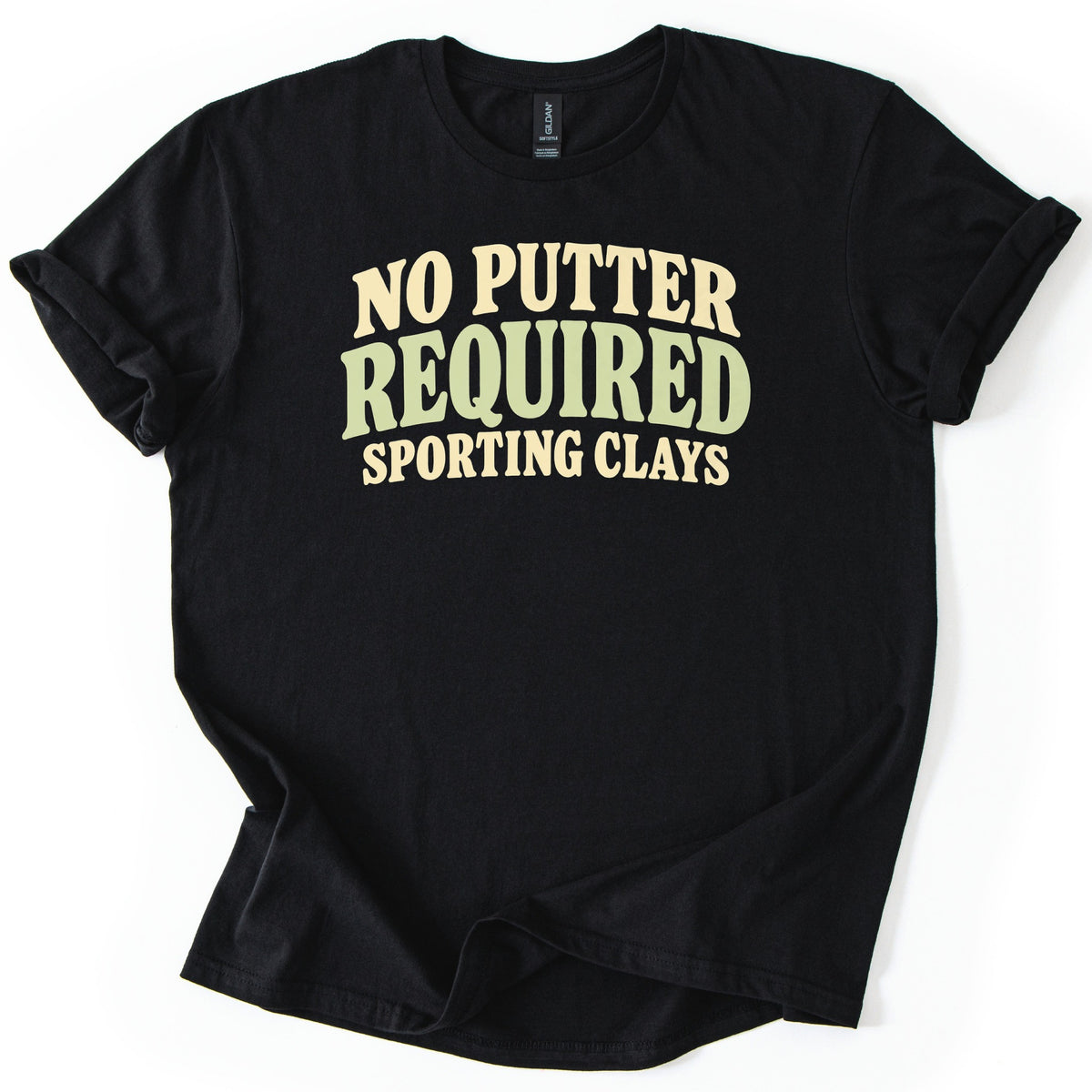 No Putter Required Comfort Colors T-shirt in Black, laid flat. Wavy retro letters read NO PUTTER in cream, REQUIRED in larger sage green, and SPORTING CLAYS in cream below. The shirt lies on a white background with its sleeves cuffed and the hem loosely folded.