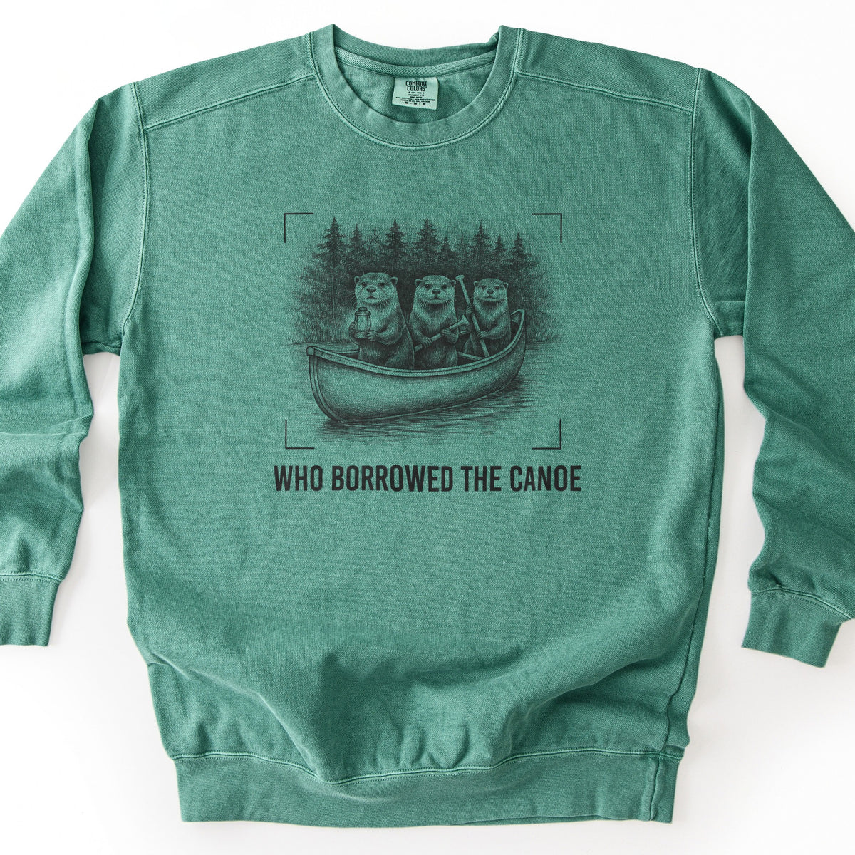 Who Borrowed The Canoe Comfort Colors crewneck sweatshirt in Light Green, laid flat. A dark sketch of three otters in a canoe, one holding a lantern and two gripping paddles, with pine trees behind and framed by corner brackets, above the words WHO BORROWED THE CANOE. Laid on a white surface.