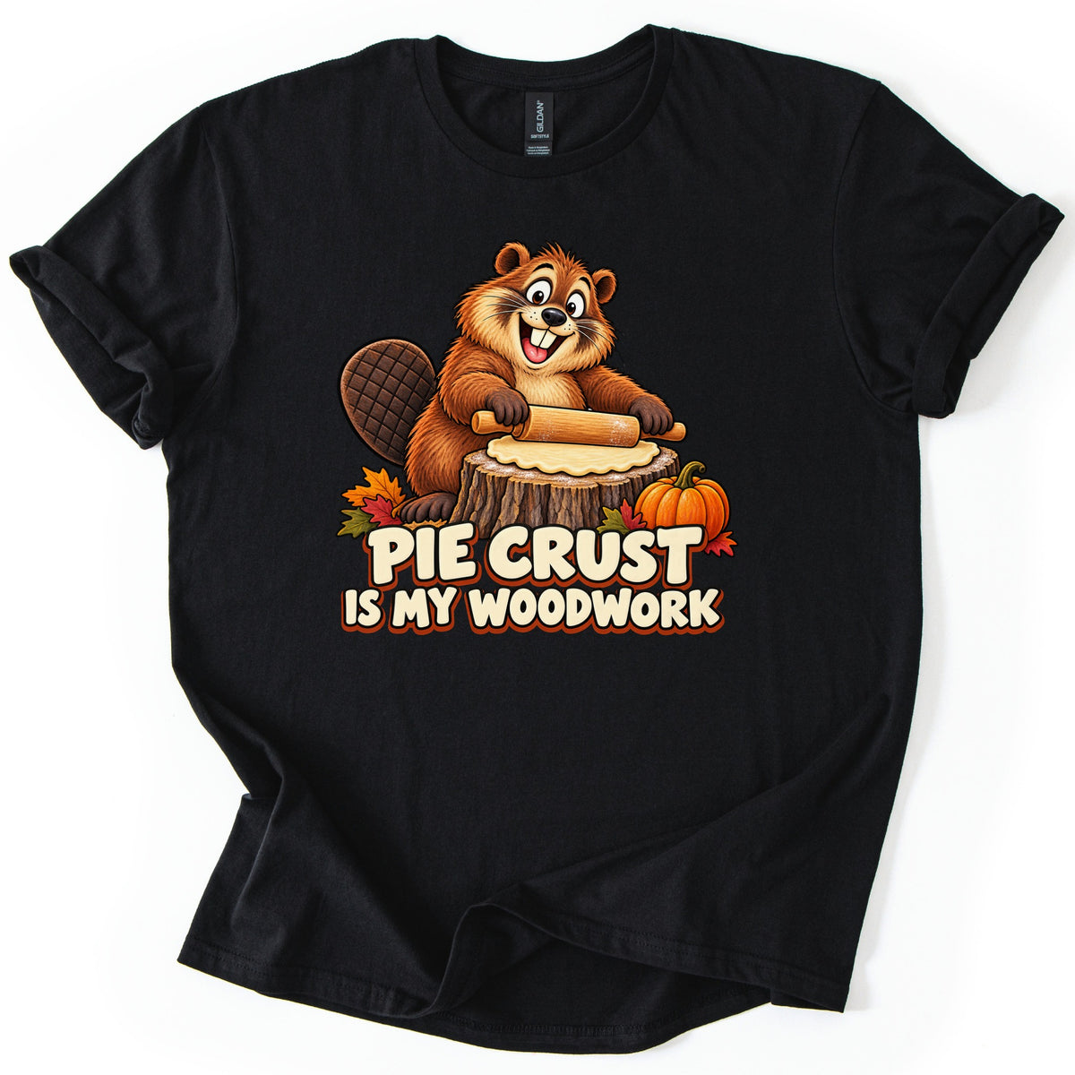 Pie Crust Is My Woodwork Comfort Colors T-shirt in Black, laid flat. A smiling cartoon beaver with a flat tail rolls out pie dough on a tree stump next to a pumpkin and fall leaves, above the words Pie Crust Is My Woodwork. Cuffed sleeves, on a white background.