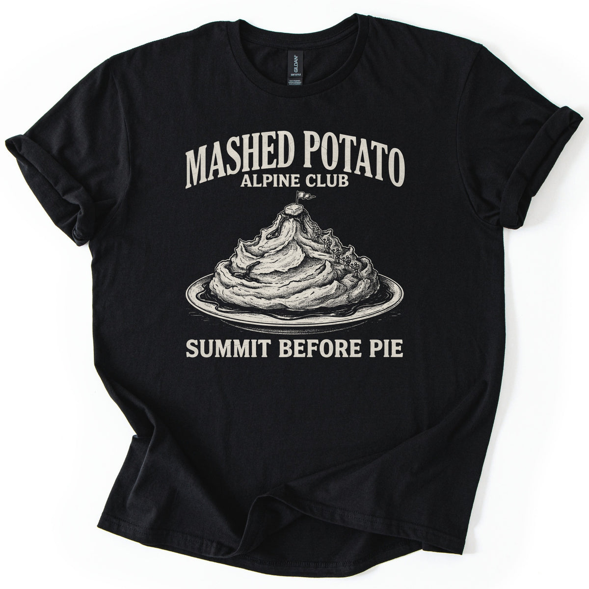 Mashed Potato Alpine Club Comfort Colors T-shirt in Black, laid flat. Cream etched art of a mashed potato mountain on a plate of gravy, with tiny climbers and a butter pat and flag on top, under Mashed Potato Alpine Club and above Summit Before Pie. Rolled sleeves, white background.