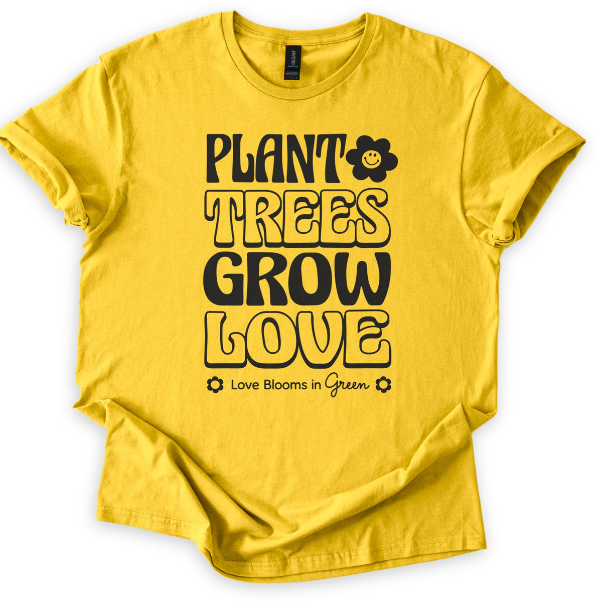 Plant Trees Grow Love Comfort Colors T-shirt in Daisy, laid flat. Black retro bubble letters read Plant Trees Grow Love, with a smiling daisy beside Plant and Love Blooms in Green between two small flowers below. Sleeves are rolled on a white background.