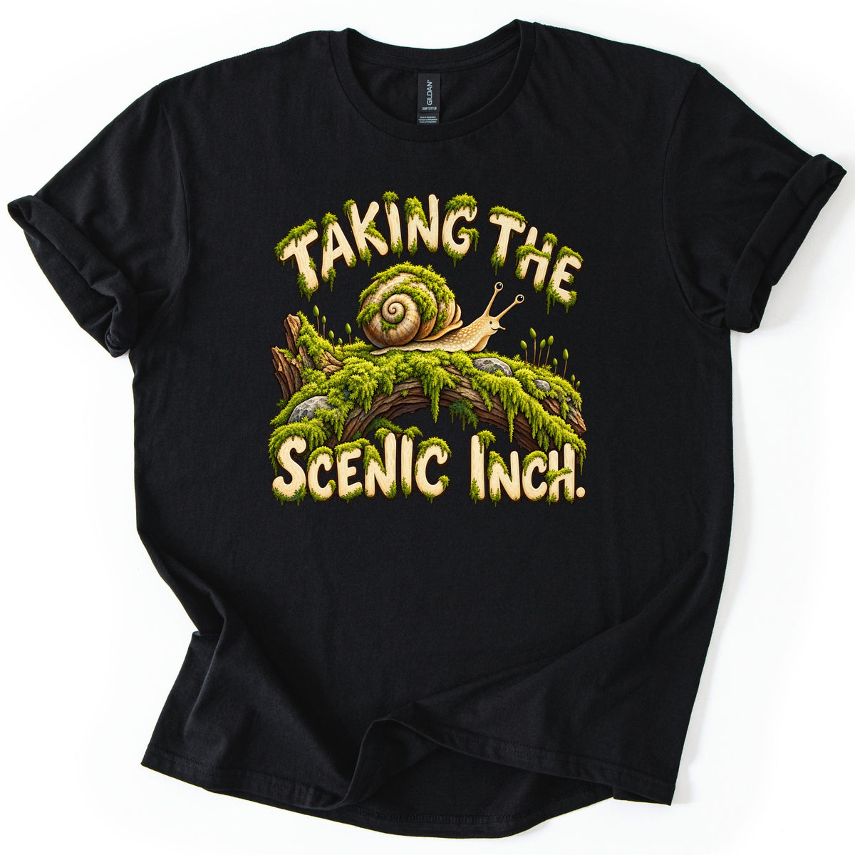 Taking the Scenic Inch Comfort Colors T-shirt in Black, laid flat. A spiral-shelled snail crawls along a moss-covered log with small rocks, between the moss-dripping words Taking the Scenic Inch. The shirt has rolled sleeves on a plain white background.