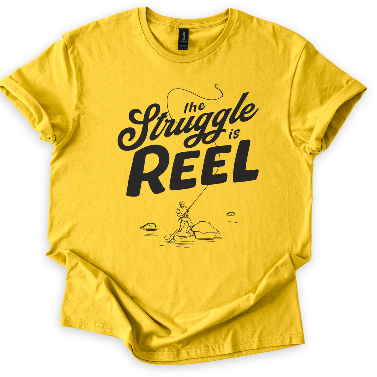 Struggle Is Reel Angler Comfort Colors T-shirt in Daisy, laid flat. Black text reads the Struggle is REEL, with a fishing line arcing over the words to a hook. Below, a line drawing of an angler in a hat casts from a rock in the water. Sleeves cuffed, on a white background.