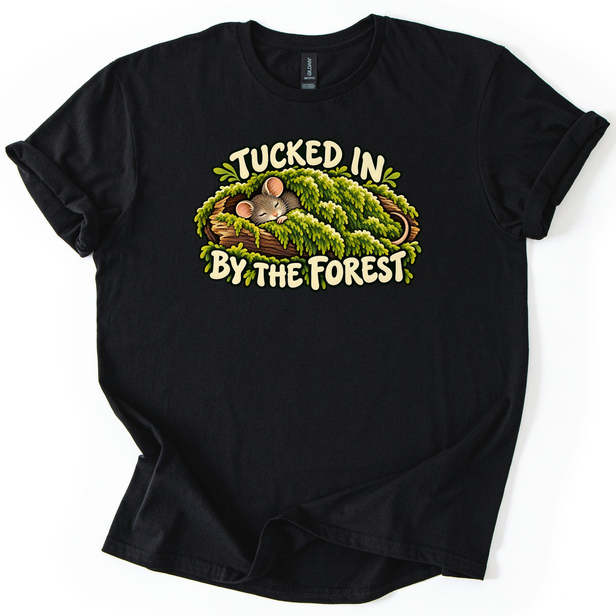 Tucked in by the Forest Comfort Colors T-shirt in Black, laid flat. A sleeping gray mouse with pink ears lies under a blanket of green moss in a hollow log, between cream words reading Tucked in By the Forest. The shirt has rolled sleeves on a white background.