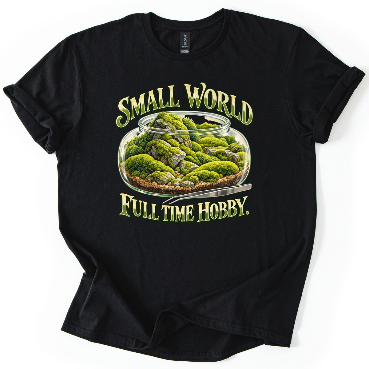Small World Full Time Hobby Comfort Colors T-shirt in Black, laid flat. A glass terrarium jar of green moss and gray rocks on gravel, with metal tweezers beside it, between the words Small World and Full Time Hobby. in green and gold letters. Sleeves cuffed, on a white background.
