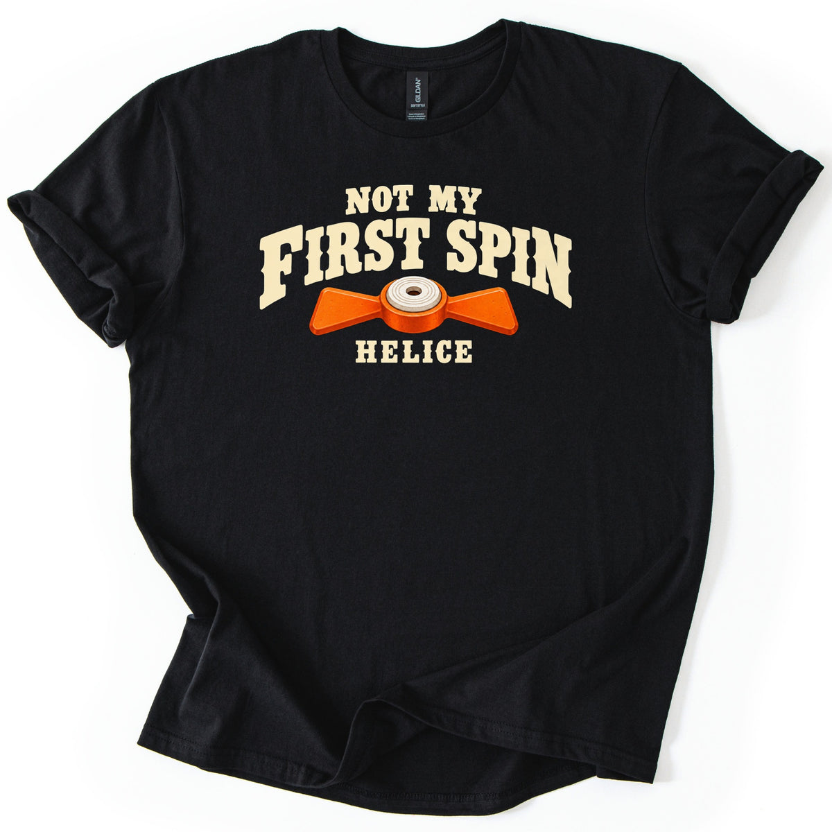 Not My First Spin Comfort Colors T-shirt in Black, laid flat. Cream western-style letters read Not My First Spin above an orange two-bladed propeller target with a white center, with the word Helice below. The shirt lies on a white surface with sleeves cuffed.