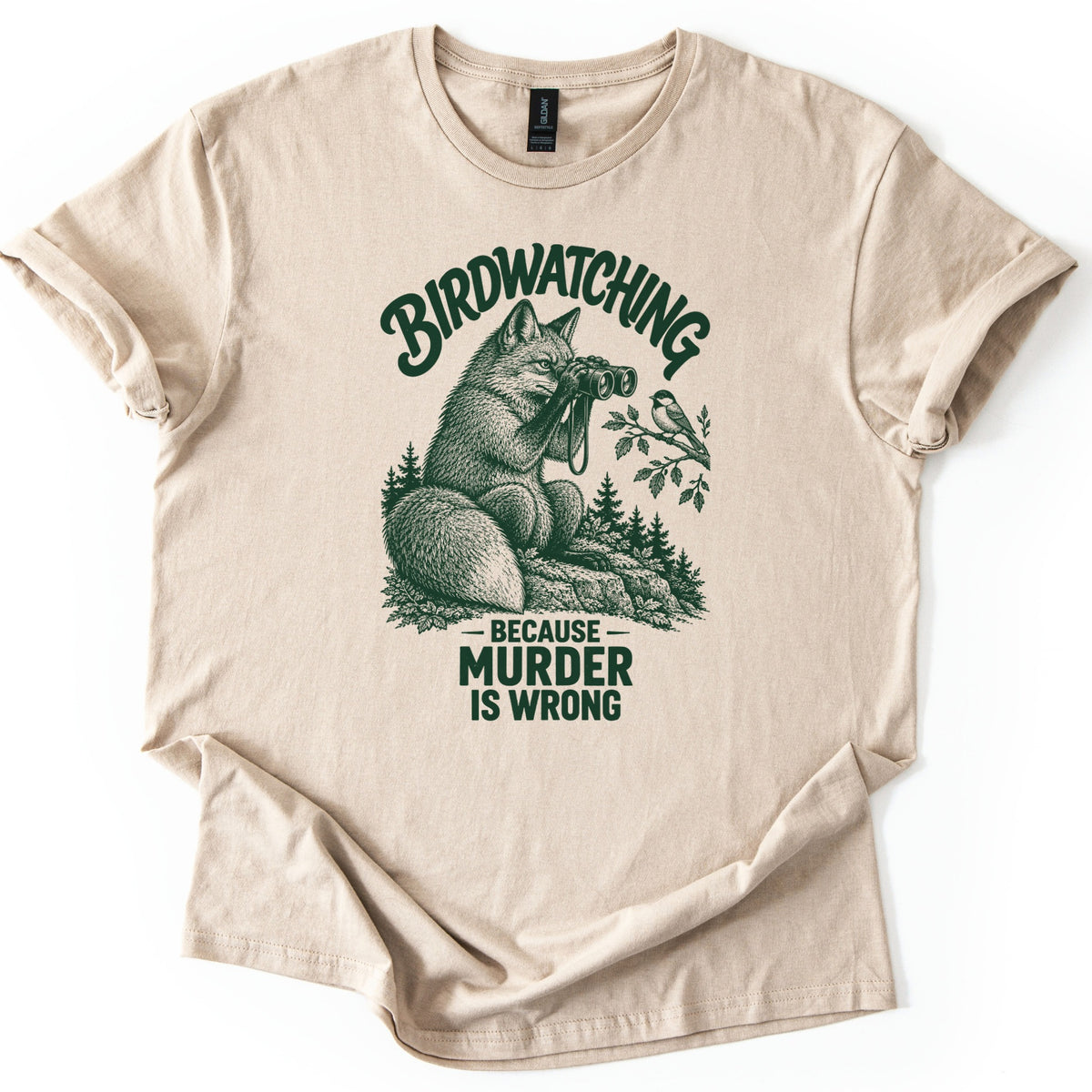 Birdwatching Murder Fox Comfort Colors T-shirt in Sand, laid flat. A sketched fox sits on a rock peering through binoculars at a chickadee on a branch, with Birdwatching arched above and Because Murder Is Wrong below, in dark green ink. On a white surface, sleeves cuffed.