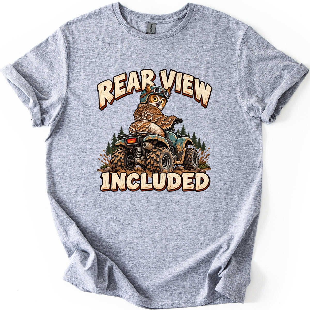 Rear View Included Comfort Colors T-shirt in Sport Grey, laid flat. A cartoon owl in a helmet and goggles looks back over its shoulder while riding a mud-splattered ATV by pine trees, between the words Rear View Included. The shirt lies on a white surface.