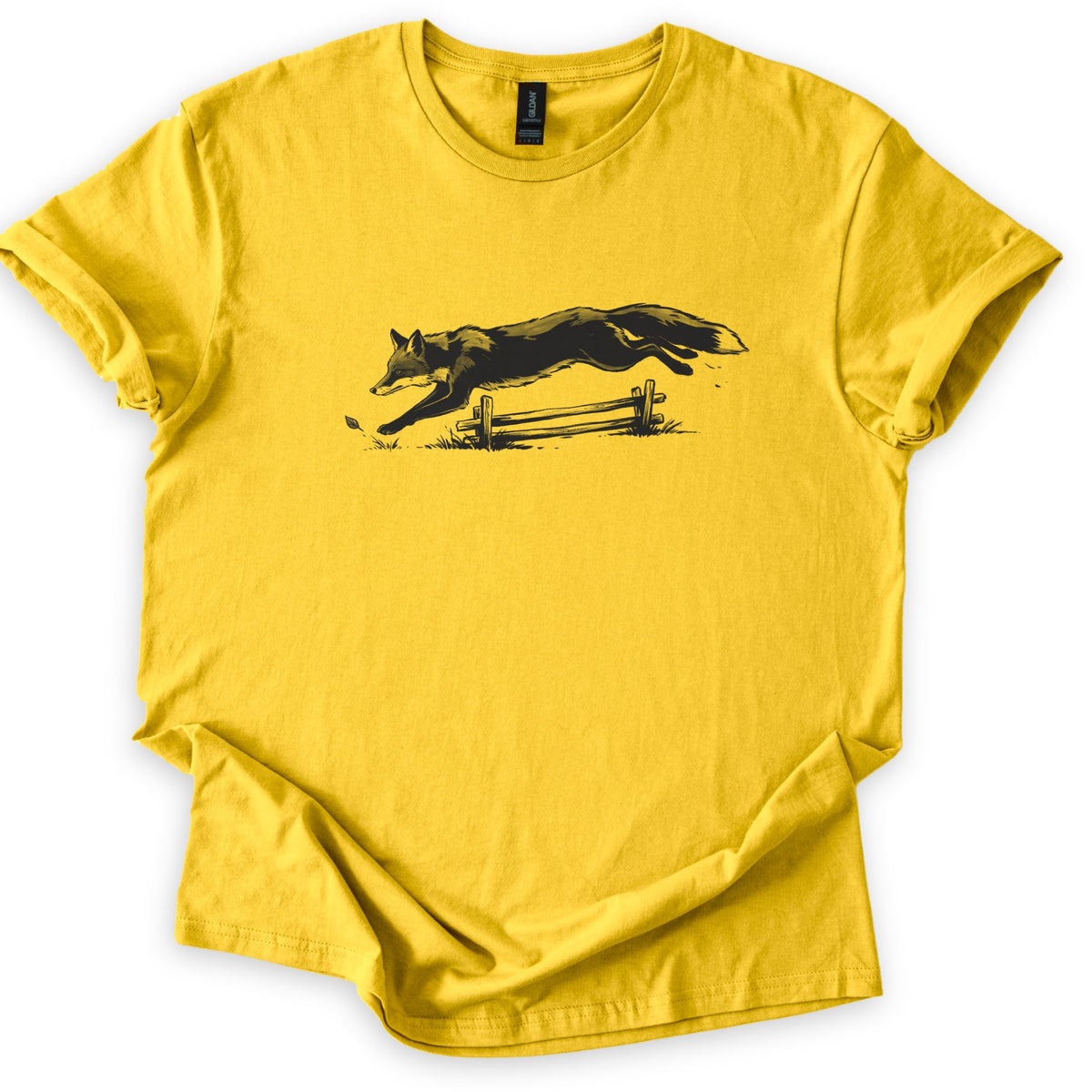 Leaping Fox Comfort Colors T-shirt in Daisy, laid flat. A black sketch of a fox leaping over a low wooden rail fence, with grass tufts and a falling leaf below. The shirt has cuffed sleeves and lies on a white background.
