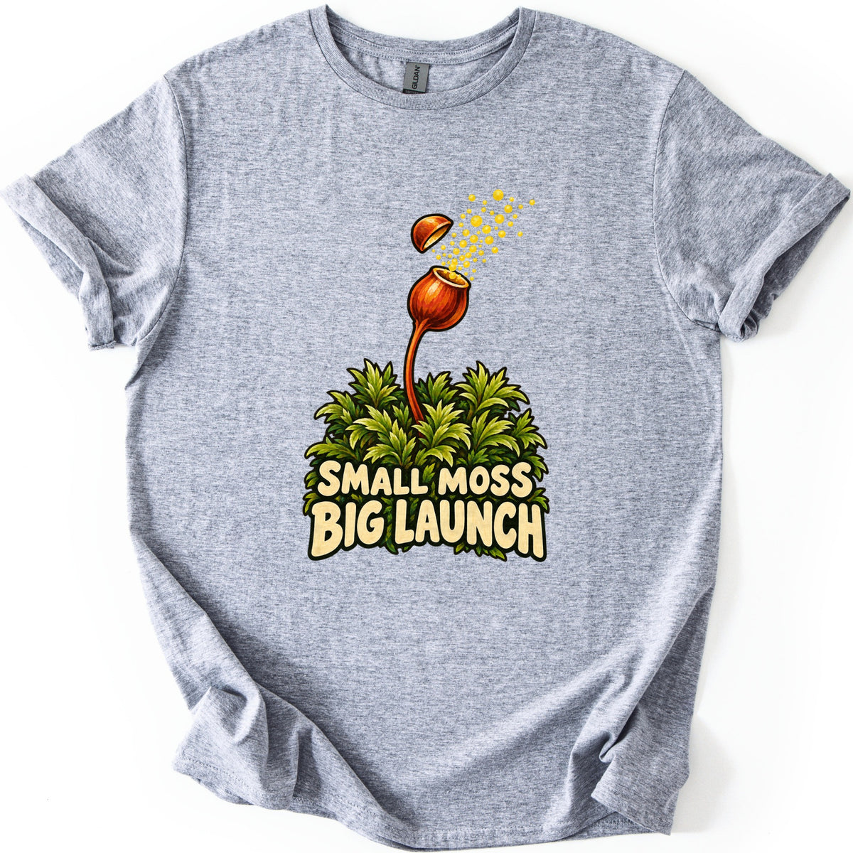 Small Moss Big Launch Comfort Colors T-shirt in Sport Grey, laid flat. An orange moss capsule on a curved stalk rises from leafy green moss, its lid popping off as yellow spores burst out, above the words Small Moss Big Launch. Rolled sleeves, on a white background.