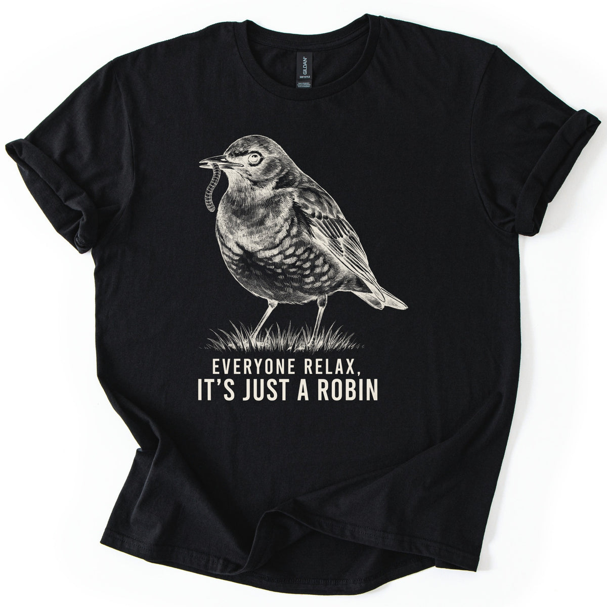 Everyone Relax It's Just A Robin Comfort Colors T-shirt in Black, laid flat. A cream sketch-style drawing of a robin holding a worm in its beak, standing on a tuft of grass, above the words Everyone Relax, It's Just A Robin. The sleeves are rolled on a white background.