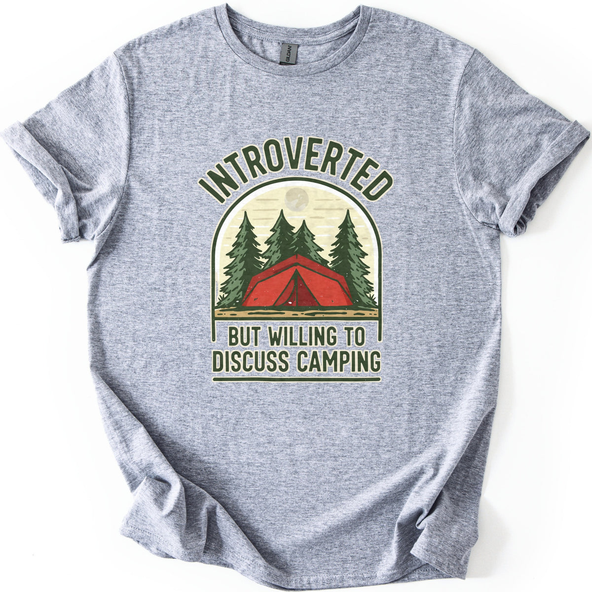 Introverted Camping Comfort Colors T-shirt in Sport Grey, laid flat. An arched badge shows a red tent among green pine trees under a pale moon, with INTROVERTED curved above and BUT WILLING TO DISCUSS CAMPING below. The shirt lies on a white background with cuffed sleeves.