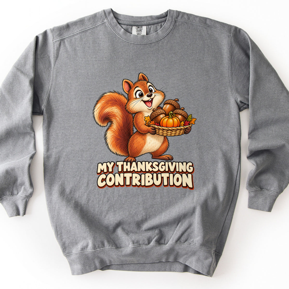 My Thanksgiving Contribution Comfort Colors crewneck sweatshirt in Grey, laid flat. A smiling cartoon squirrel holds a woven basket of acorns, a small pumpkin, and autumn leaves above the words My Thanksgiving Contribution in cream letters. Shown on a plain white background.